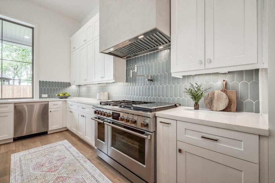 Contemporary kitchen featuring white cabinetry and a curved blue tile backsplash with double ovens