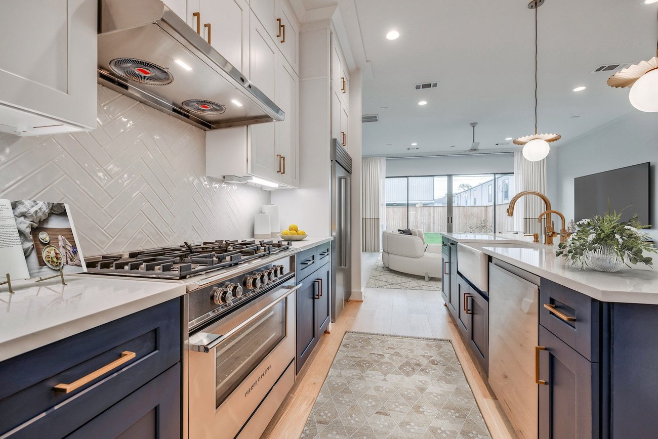 Open-concept kitchen with navy lower cabinets, white uppers, and herringbone tile backsplash