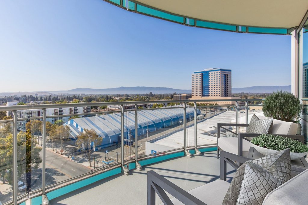 Virtually staged balcony with modern outdoor chairs, throw pillows, and a view of the city skyline