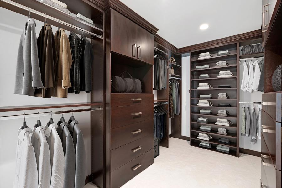digitally staged Sophisticated dark wood closet with built-in drawers, hanging rods, and folded wardrobe items.