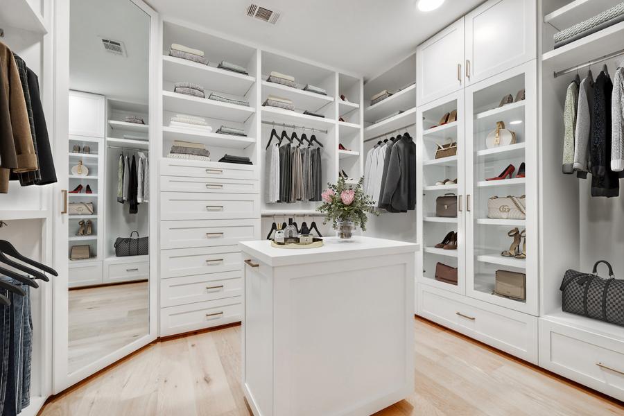 digitally staged Expansive white dressing room with dual islands and open shelving for bags and shoes.