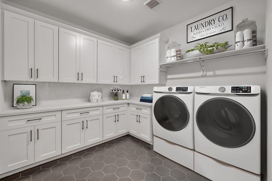 digitally staged Bright white laundry room with hex tile flooring, upper cabinets, and front-load appliances.