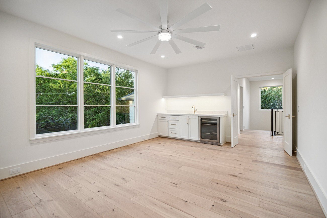 Empty contemporary room with light wood floors, white cabinetry, and large windows before virtual staging.