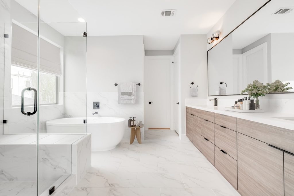 Virtually staged modern bathroom featuring marble tile, wood grain vanity, and a standalone bathtub