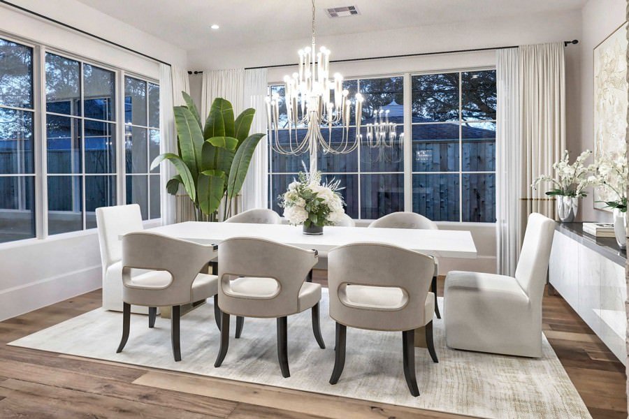 Luxury dining space featuring a grand chandelier, white table, and large windows with elegant drapery and garden views.
