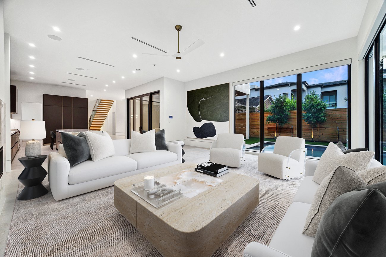 Virtual staging of a modern open living room with white curved sofas, beige stone coffee table, abstract wall art, and large windows facing a pool