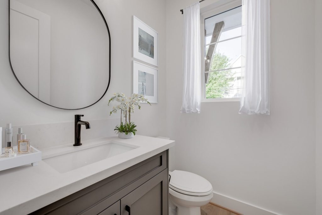 Digitally staged powder room with round mirror, orchid arrangement, and bright white decor