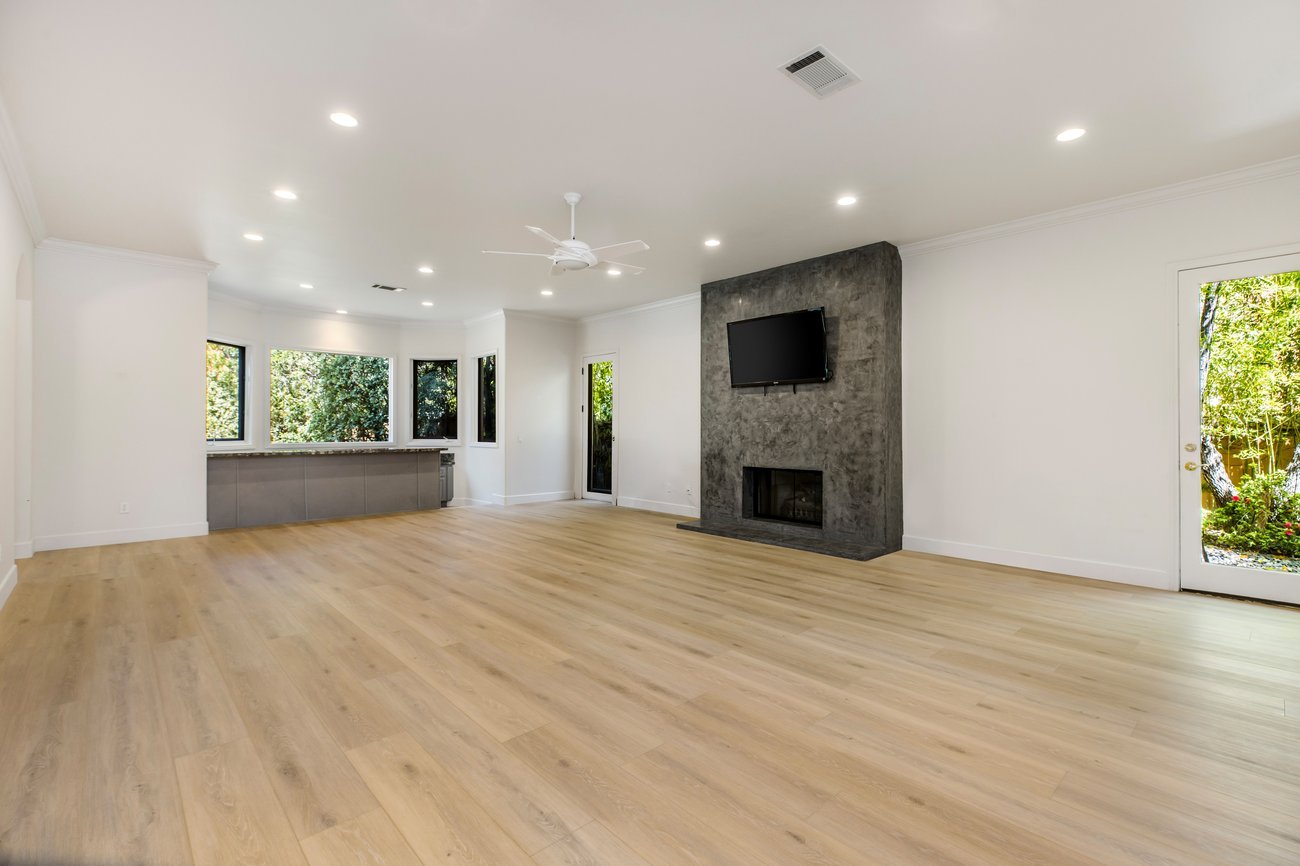 Unfurnished open-concept great room with concrete fireplace, wood flooring, and natural light