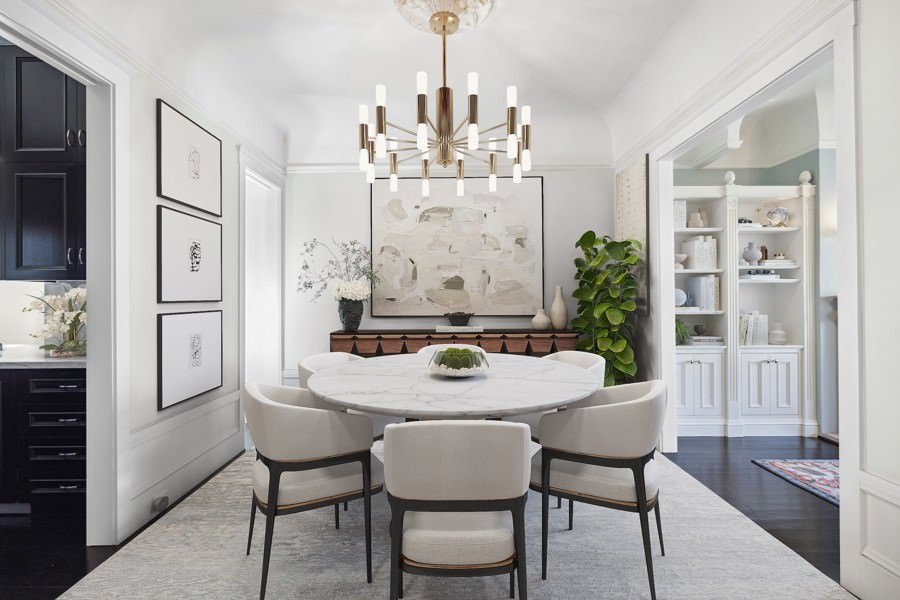 Sophisticated dining space with a rounded marble table, contemporary chandelier, and abstract artwork in black and white tones.