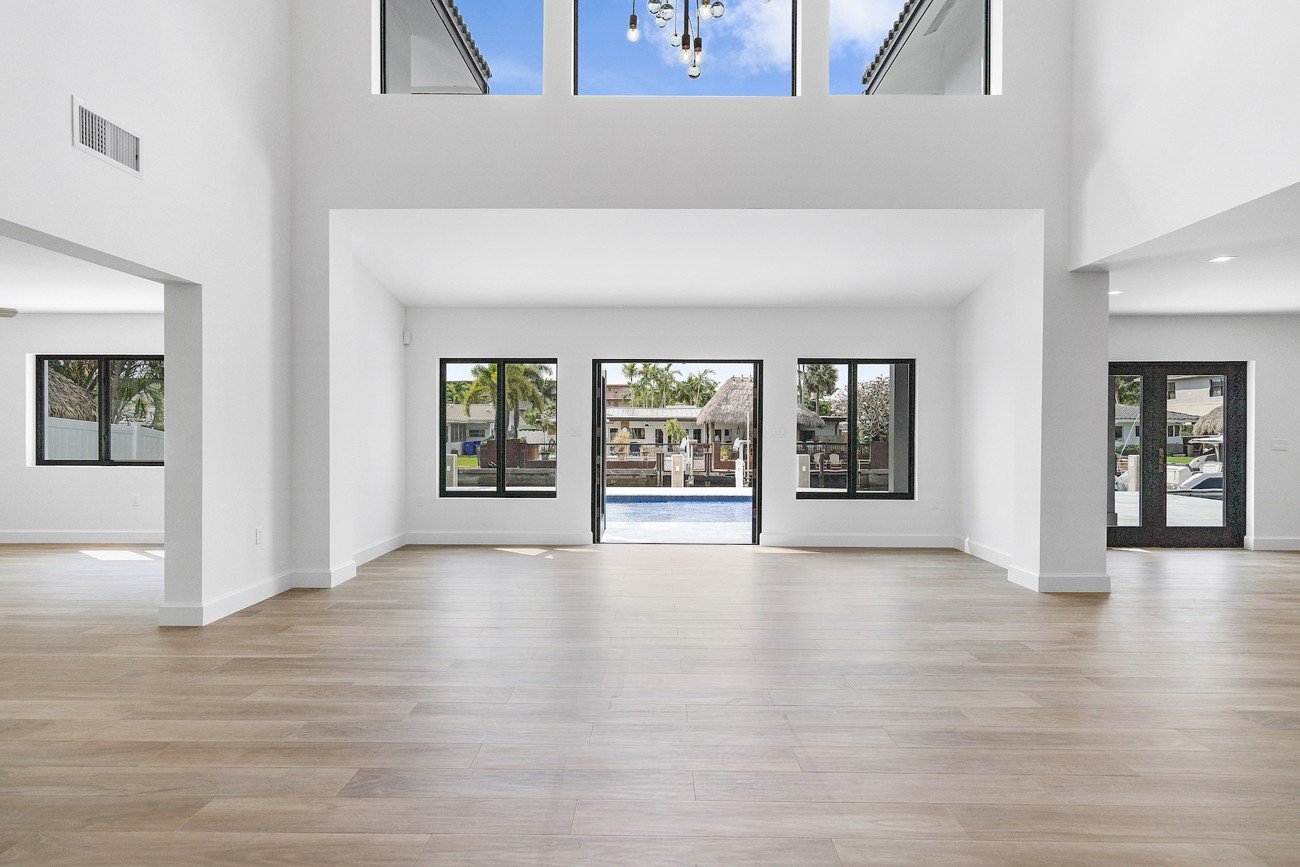 Open and spacious living area with light wood flooring, white walls, and large windows offering a pool view — shown before virtual staging.