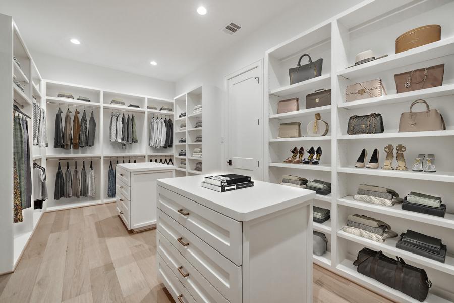 virtually staged Custom white walk-in closet with island, glass cabinets, and built-in shelving.